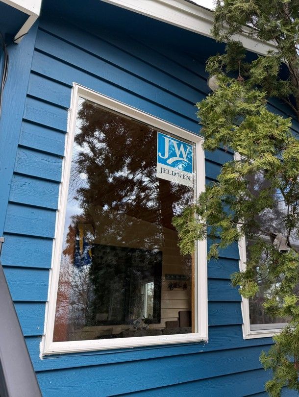 Blue house exterior with a white-trimmed window and a JW sign reflected in the glass