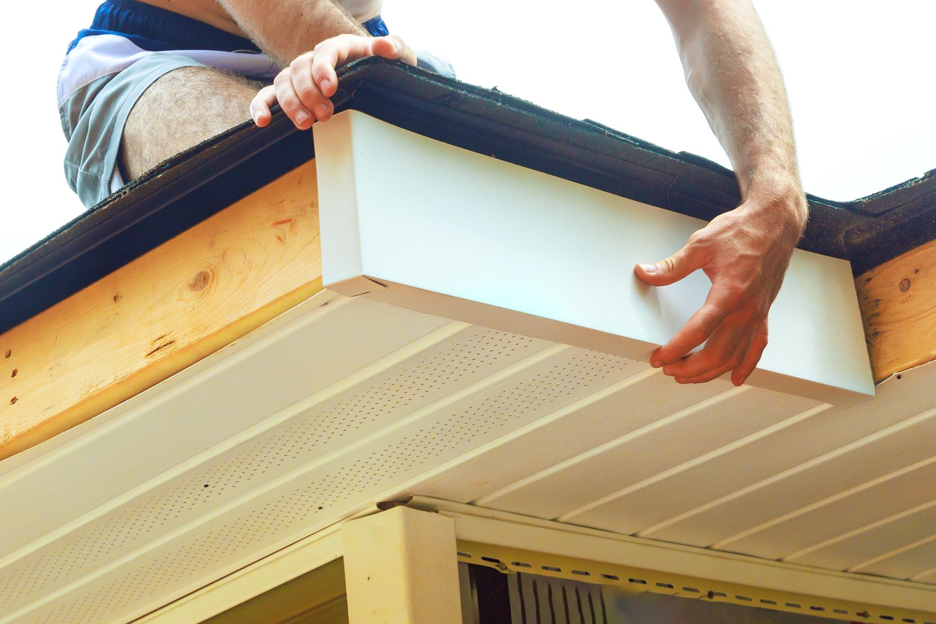 Worker installing white soffit panels under a roof overhang