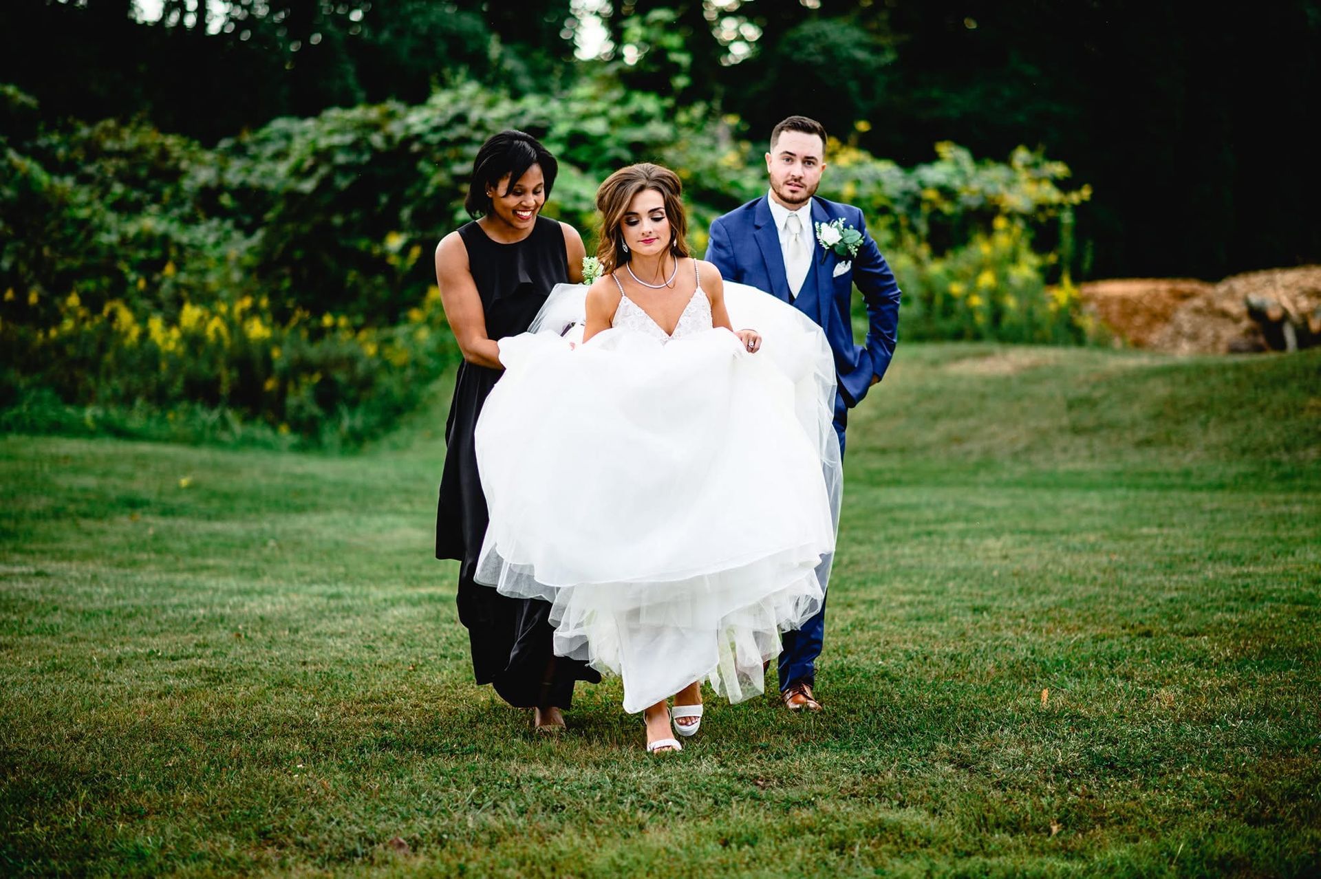 Wedding Planner Charleston WV assisting bride across the grass with wedding gown