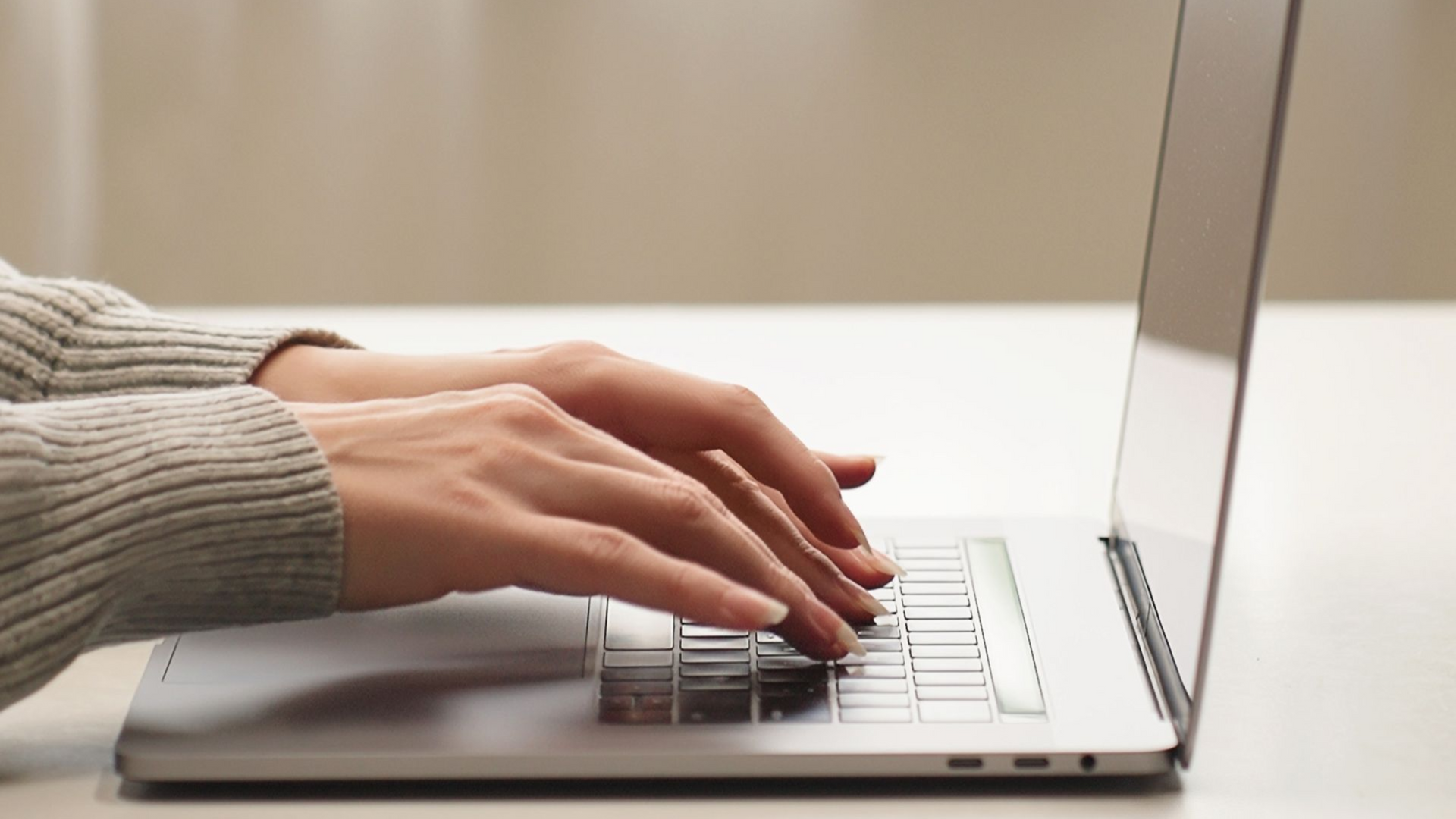 Hands typing on a silver laptop at a desk.