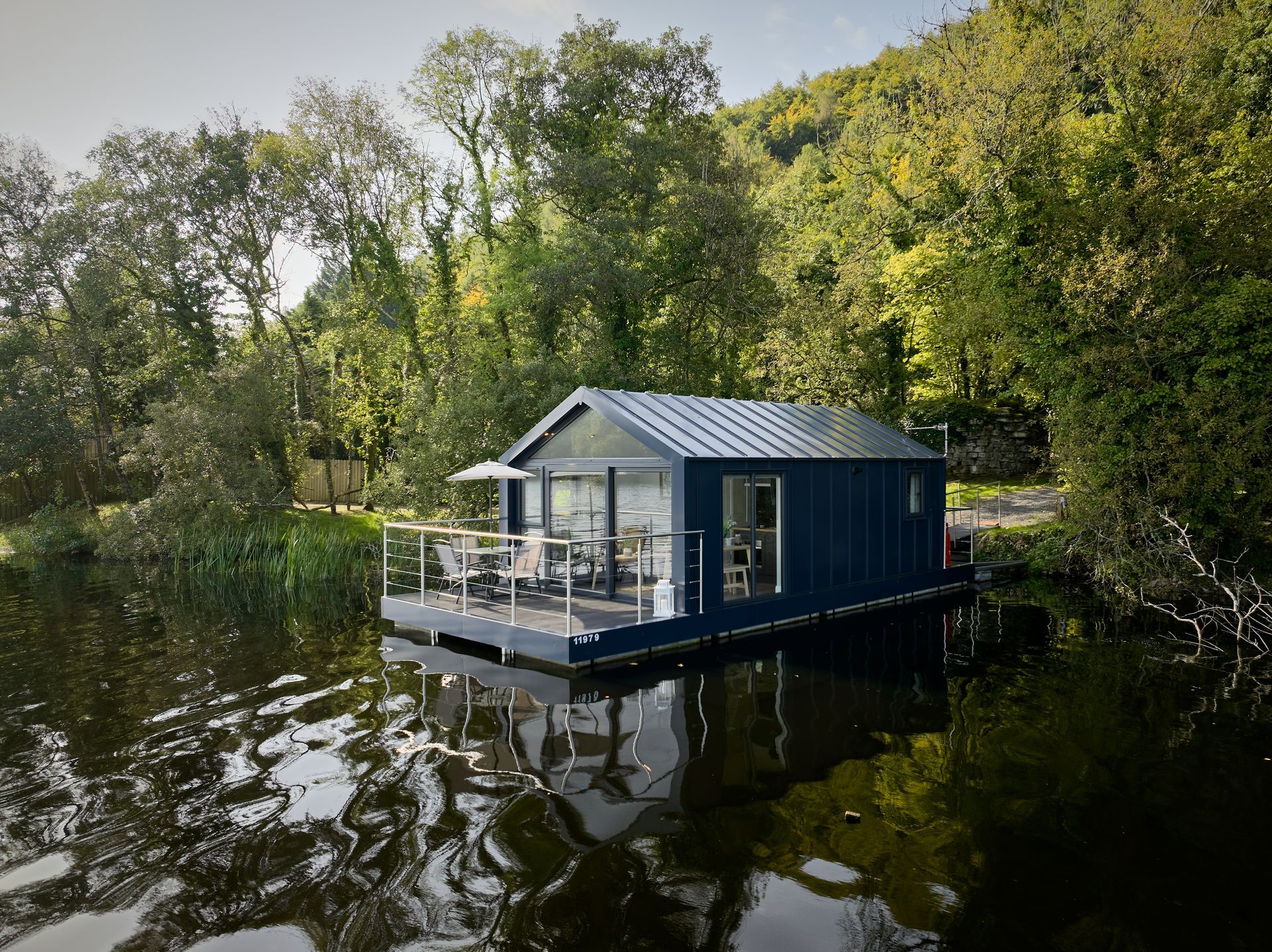 A small house is floating on top of a body of water surrounded by trees.