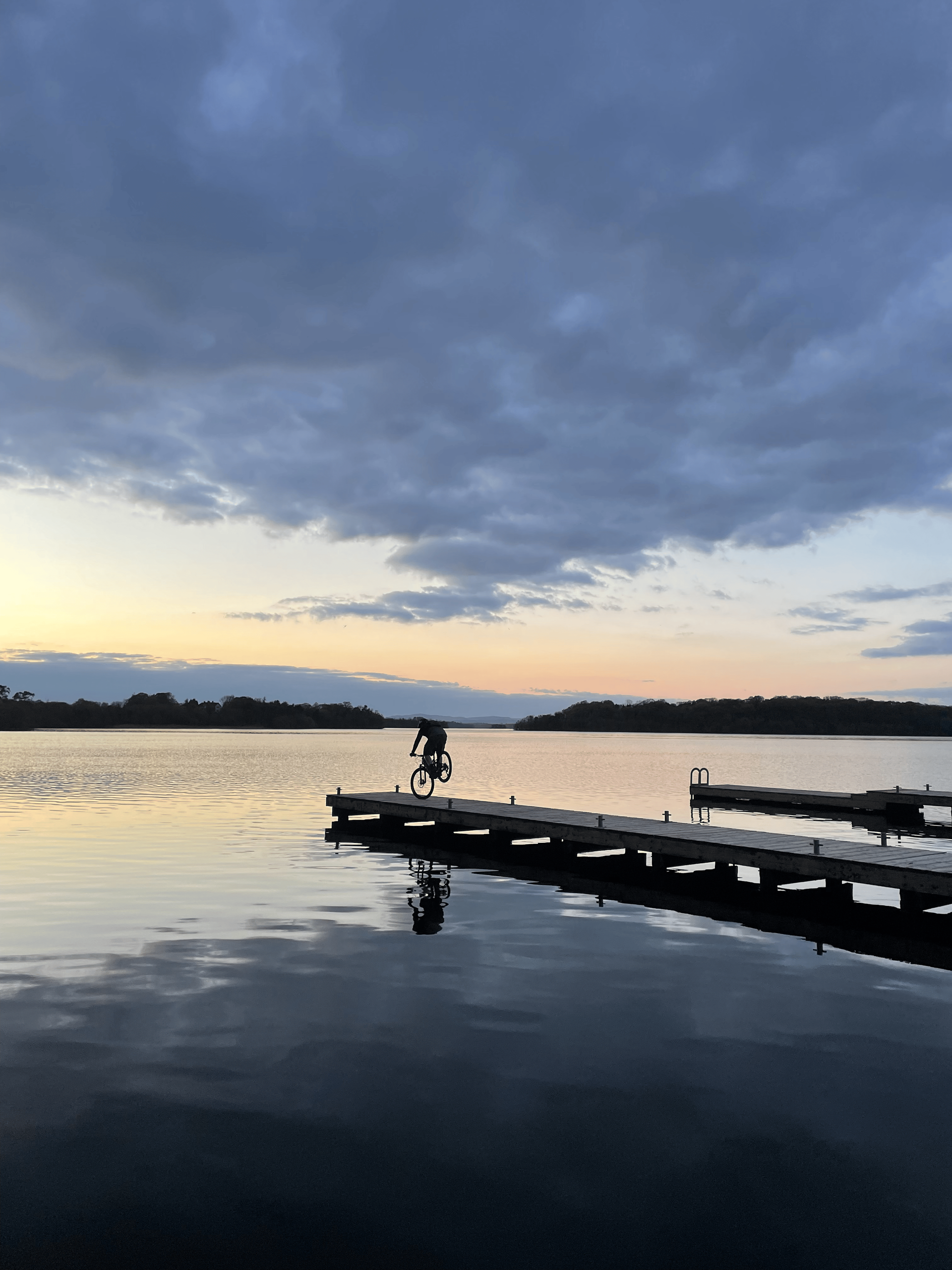 A person is standing on a dock overlooking a lake at sunset.