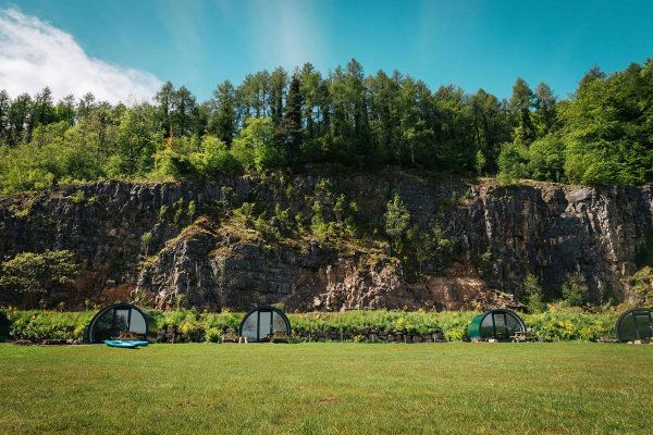 A group of tents are sitting in a grassy field in front of a mountain.
