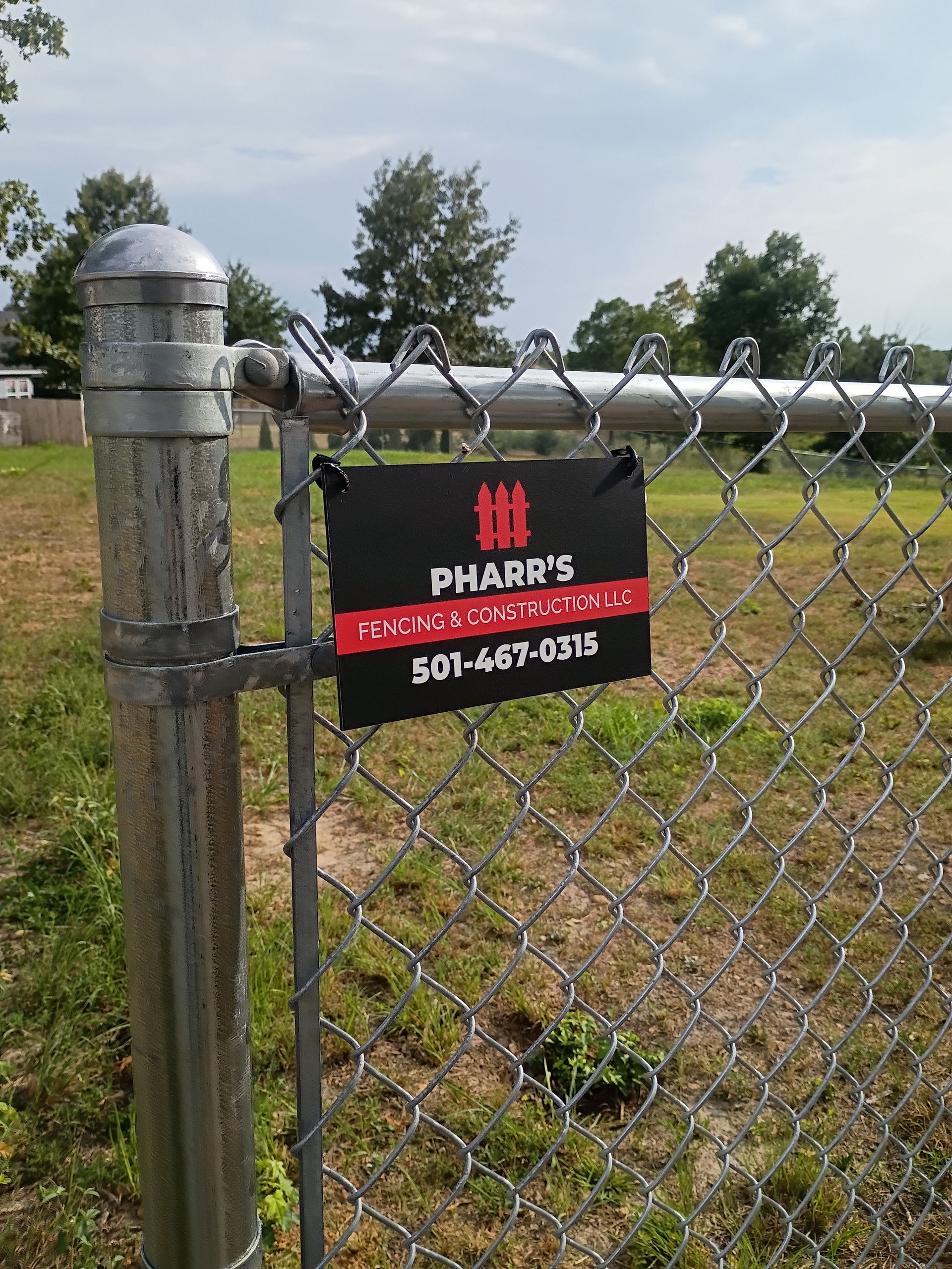 Chain-link fence with a black and red “Parks” sign and phone number in a grassy field.