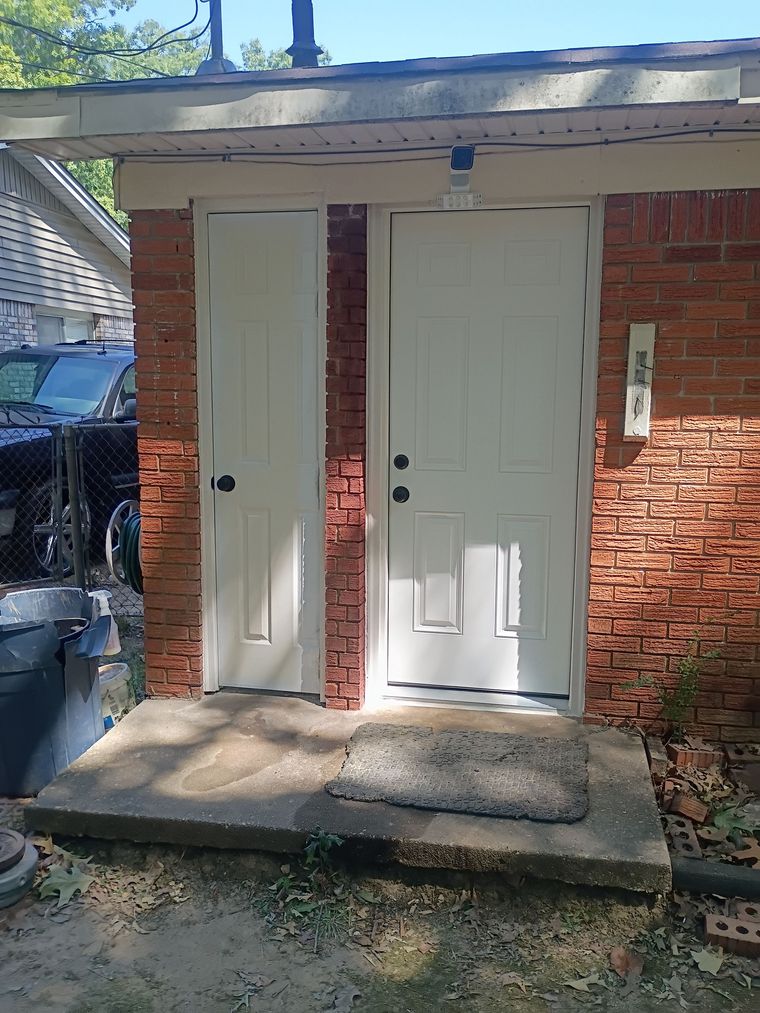 White door and side utility door on a brick house entrance with concrete steps and small porch.