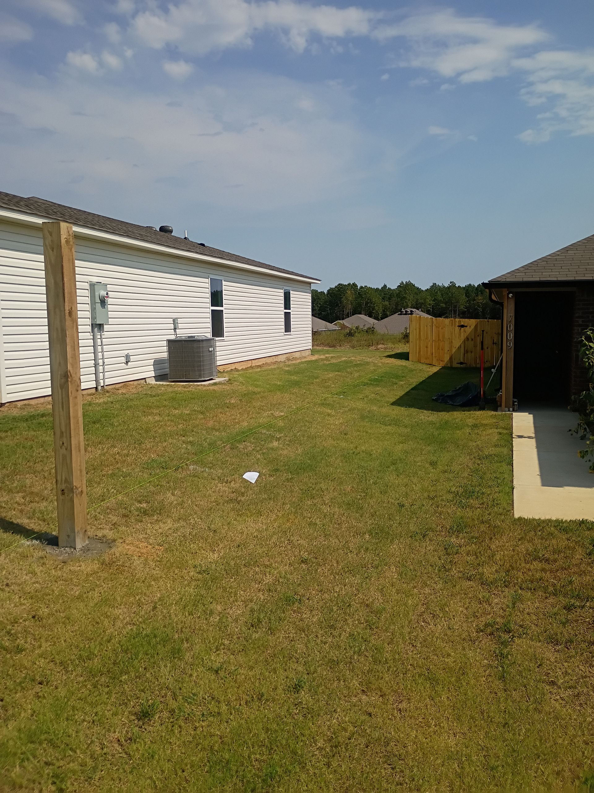 Backyard with white house, grassy lawn, wooden fence, and a small shed on a sunny day