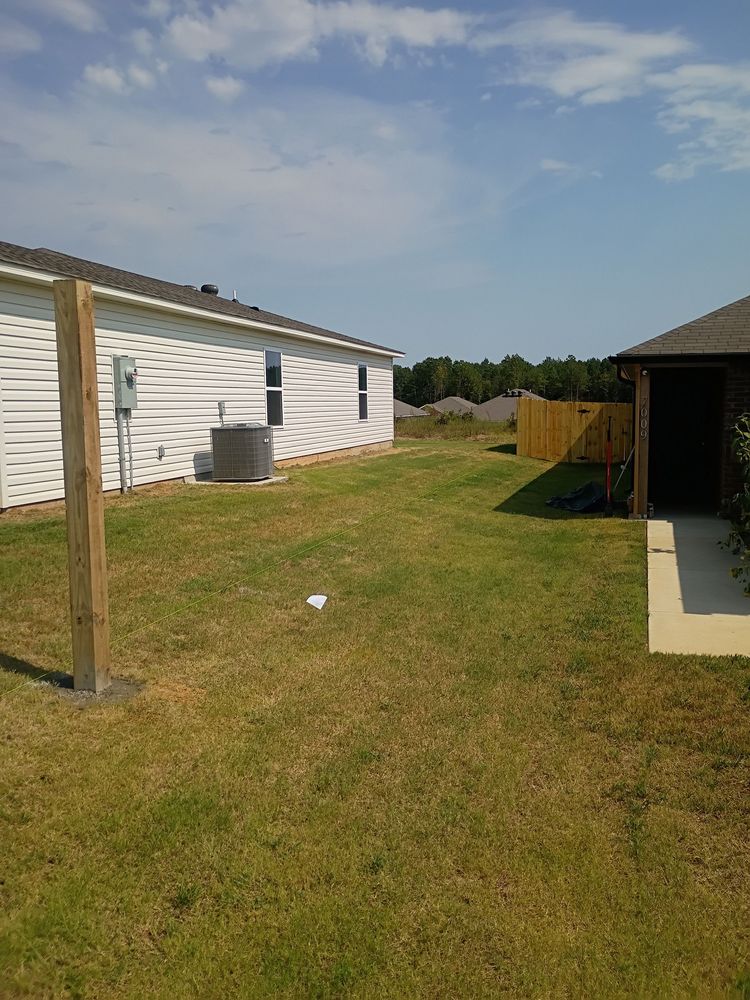 Backyard with white house siding, grassy lawn, wooden fence, and a small covered patio on the right