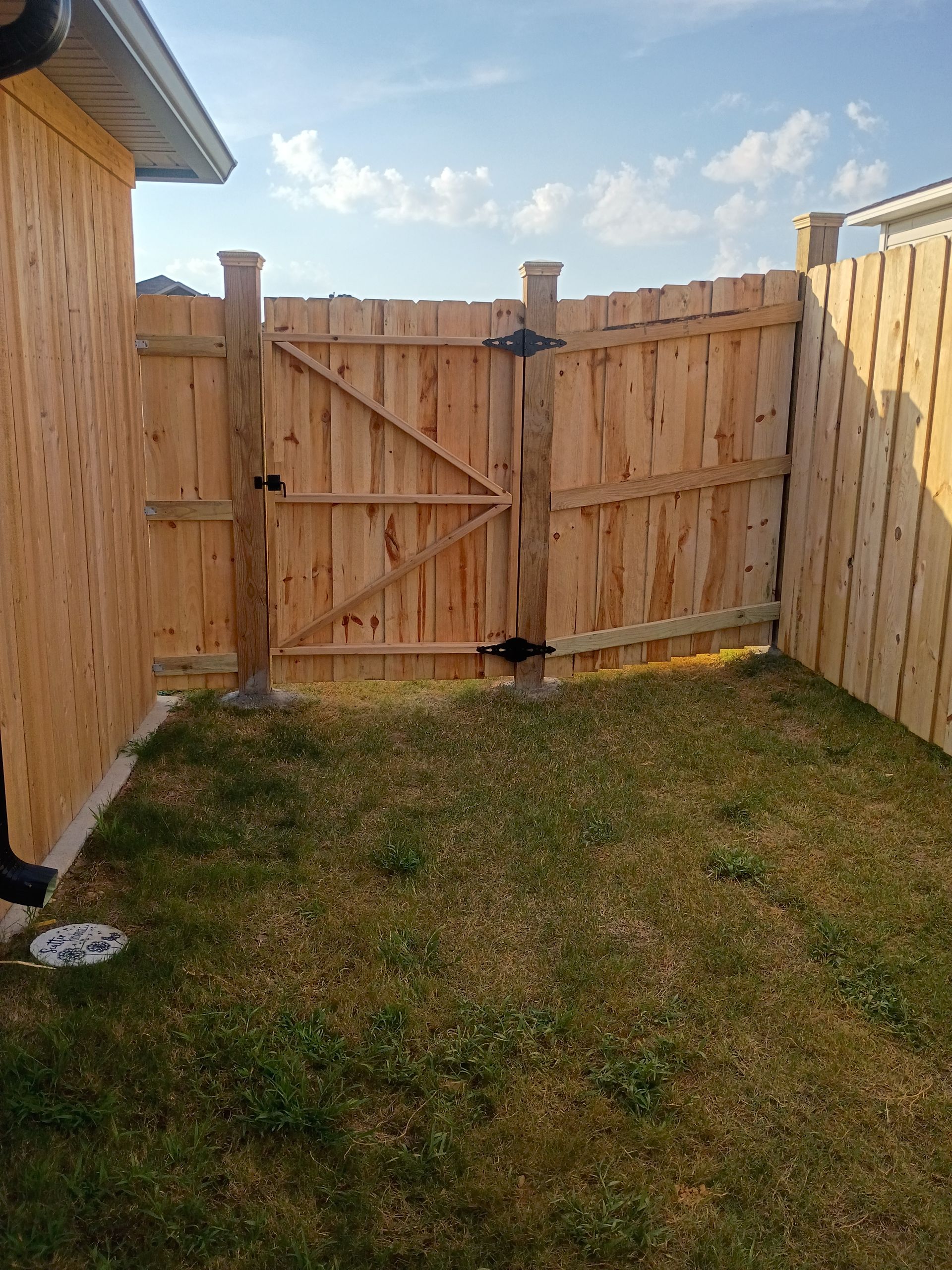Small grassy backyard with a wooden fence and closed gate under a partly cloudy sky.