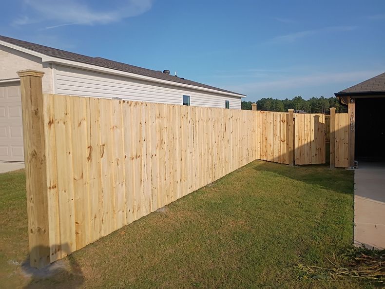 Wooden privacy fence along a suburban house and driveway under a clear blue sky