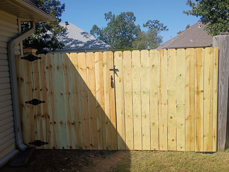 Wooden fence gate under construction beside a house in a sunny yard