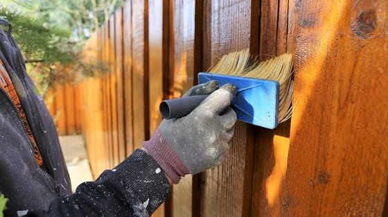 Gloved hand sanding a wooden fence panel with a blue sanding block