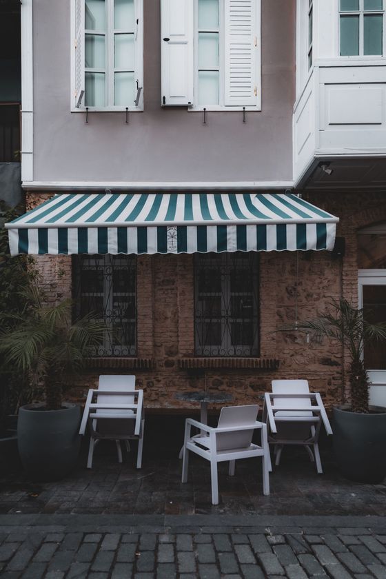 Small café facade with striped awning and white chairs on a cobblestone street.
