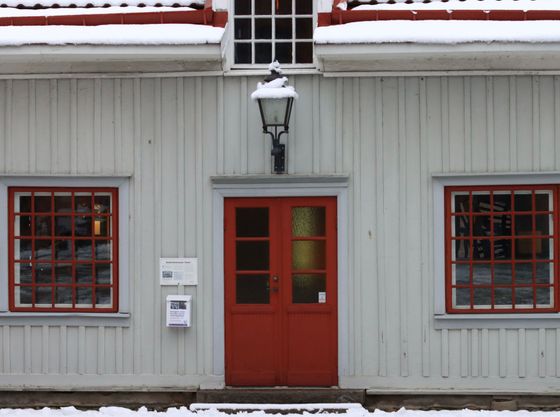 Snow-dusted red door and windows on a white building facade with a wall lantern and mailbox
