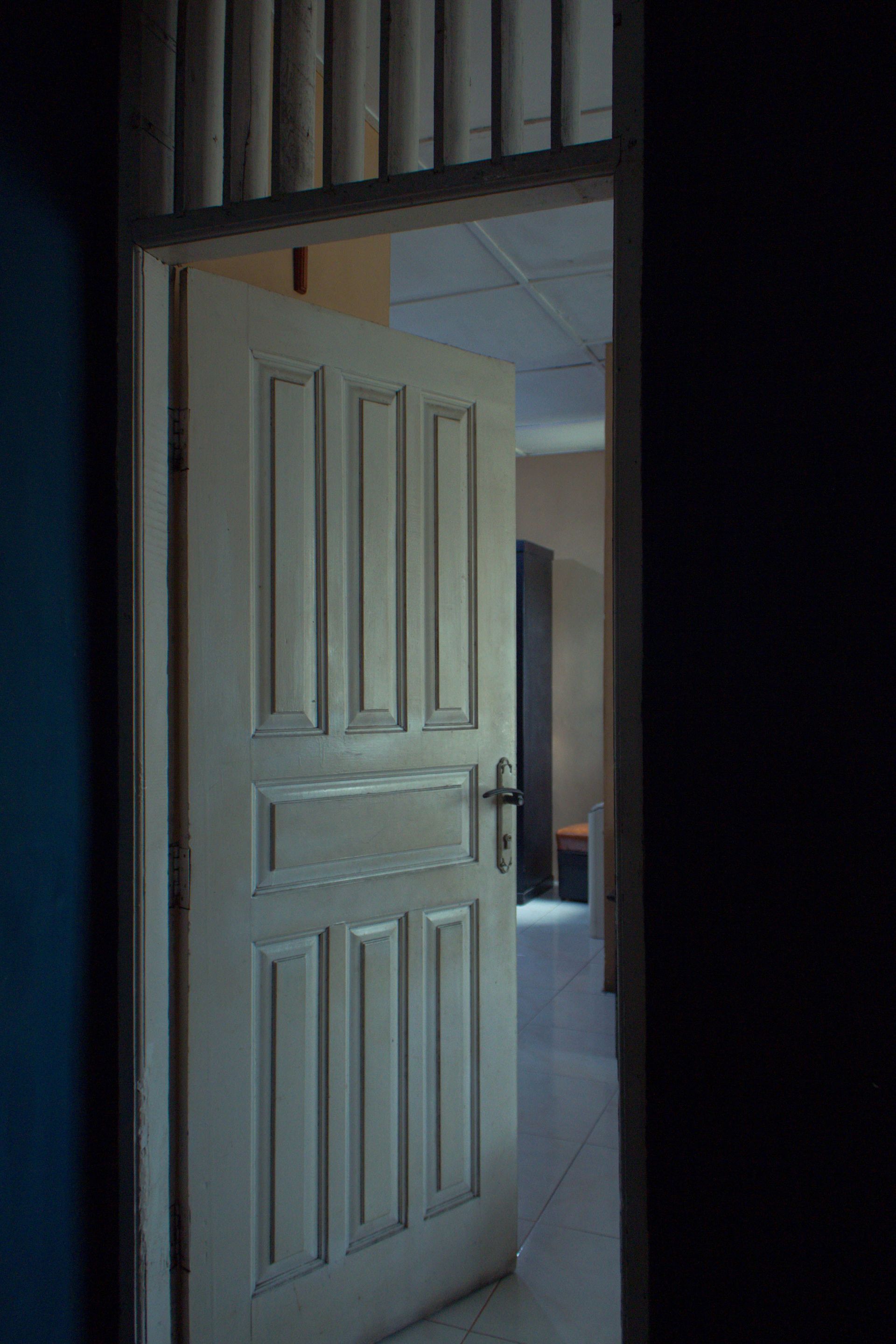 Partially open white paneled door leading to a dim room