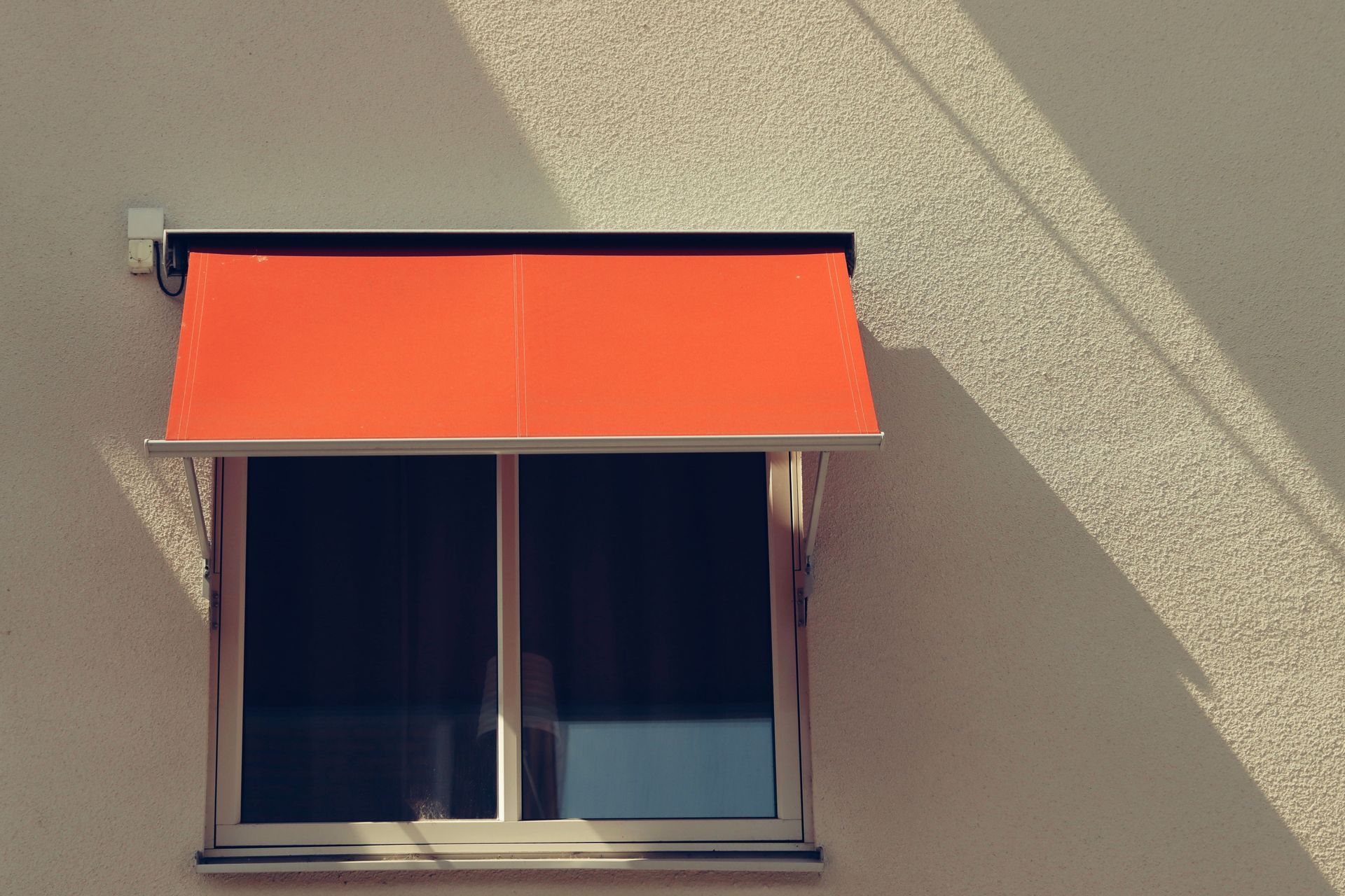 Orange awning over a small window on a beige building wall