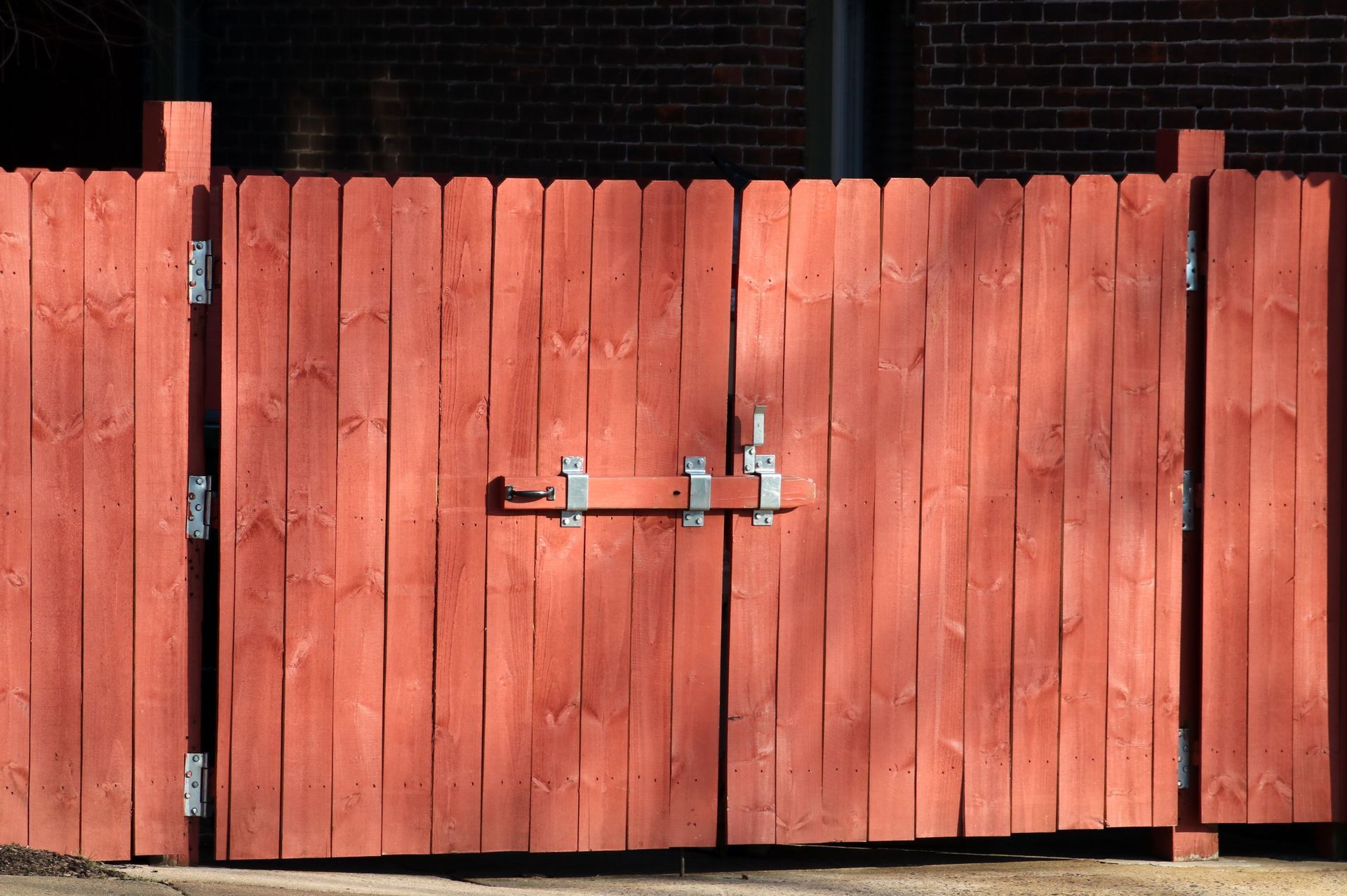 Red wooden double gate with metal latch and hinges in front of a brick wall