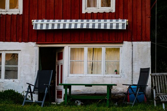 Red and white house facade with a window, bench, and chairs on a grassy yard