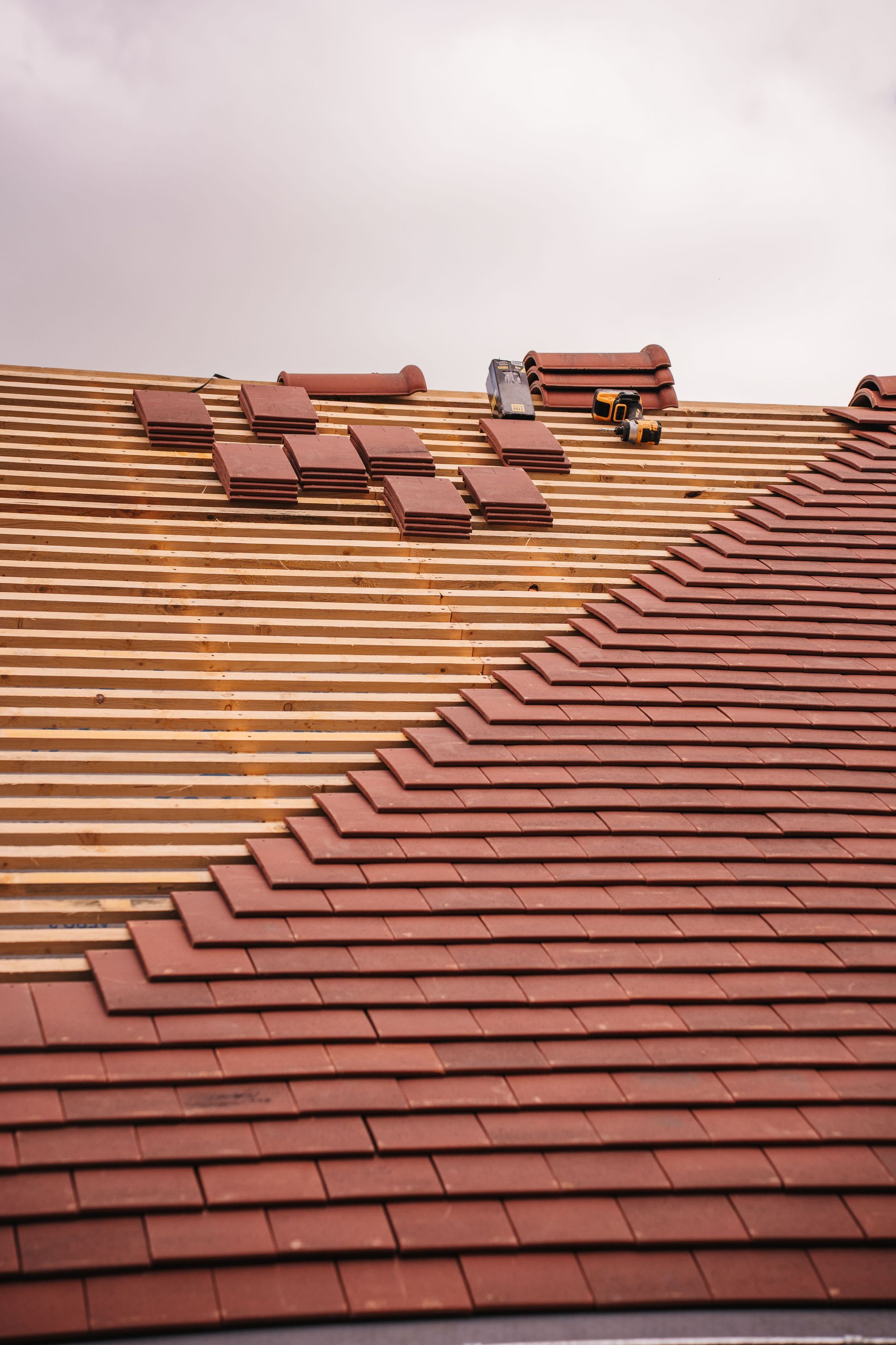 Red roof with scattered loose tiles and a damaged section near the ridge under a cloudy sky