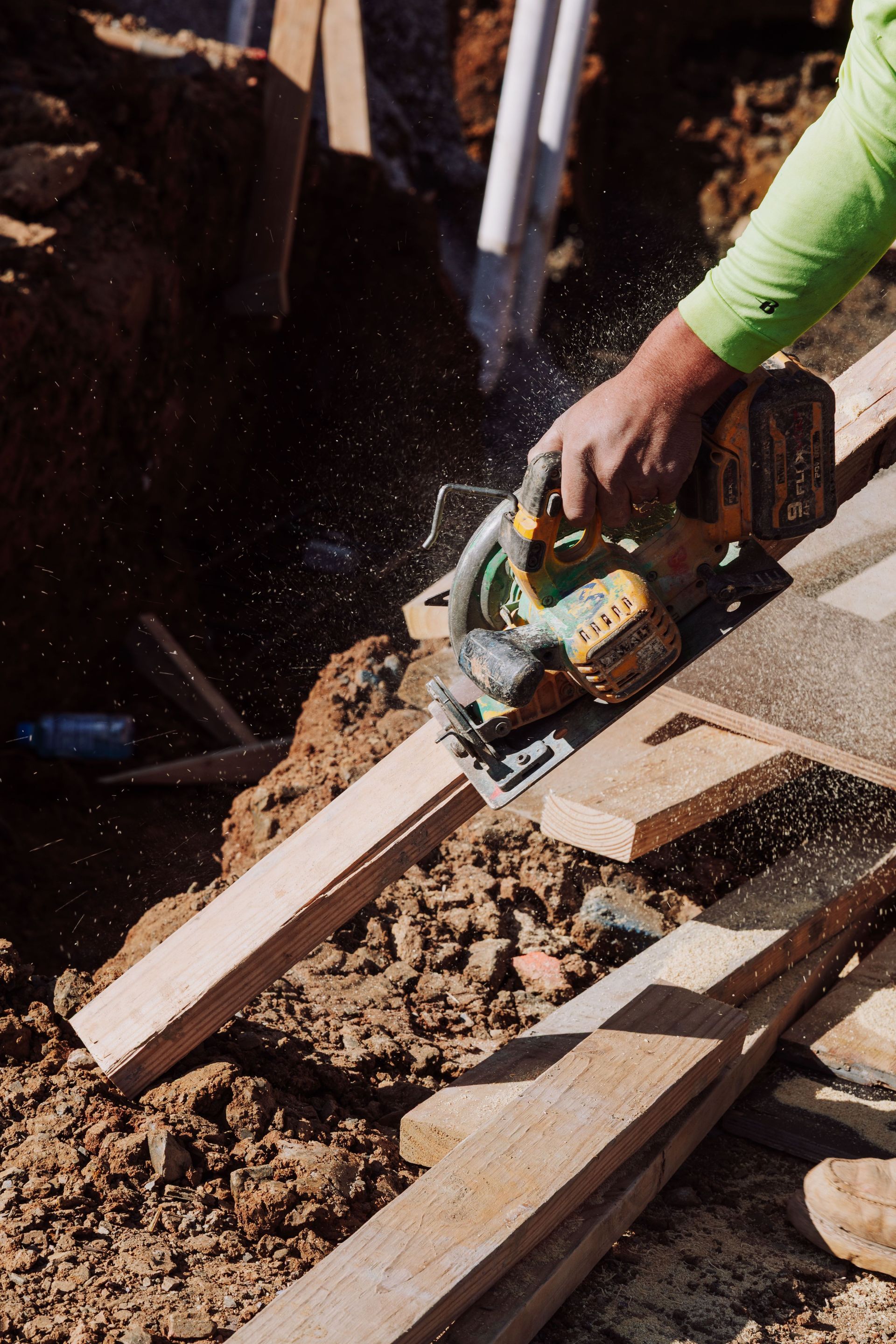 Person cutting a wooden plank with a circular saw, sending sawdust into the air.