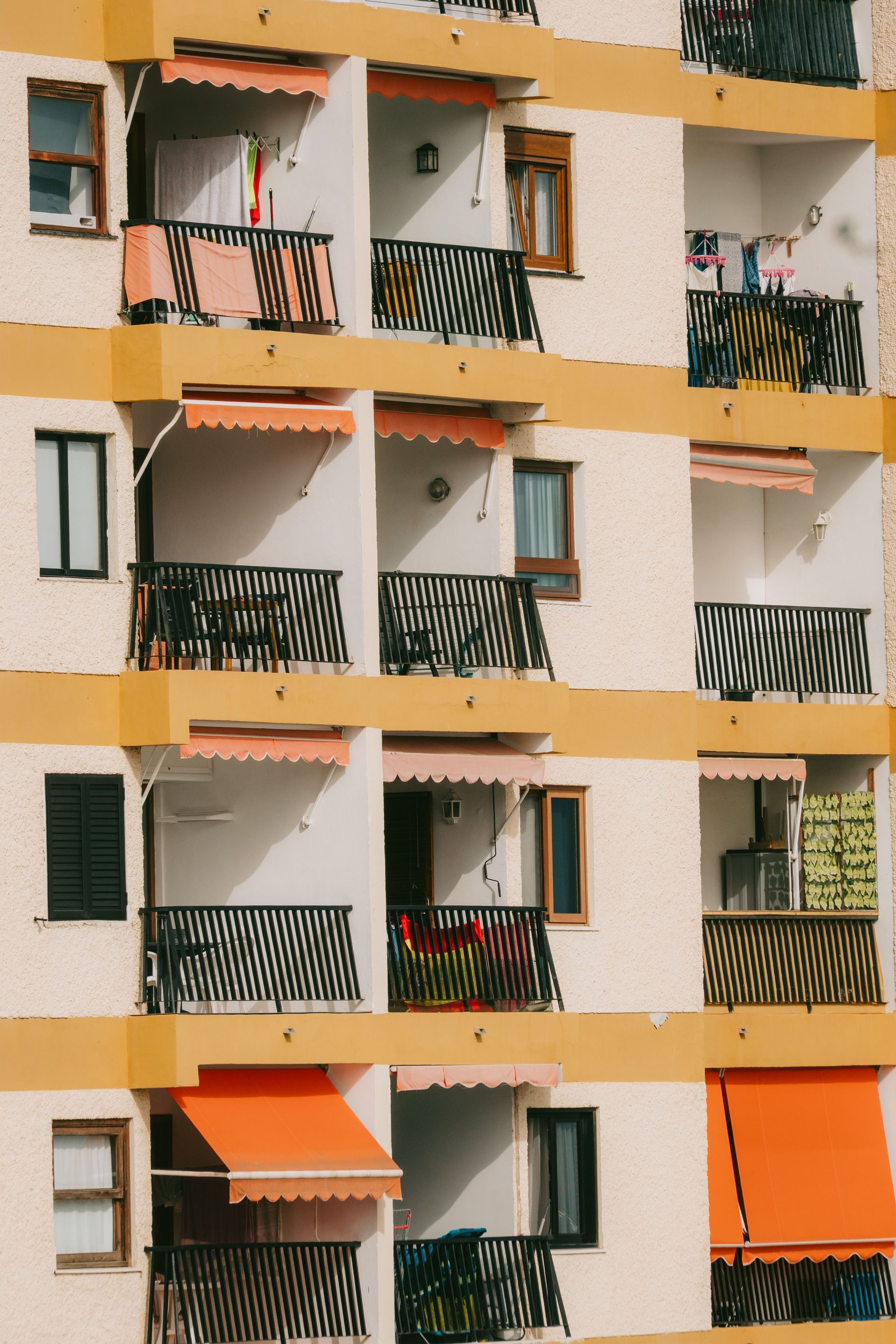 Apartment building balconies with black railings and orange awnings in a striped facade.