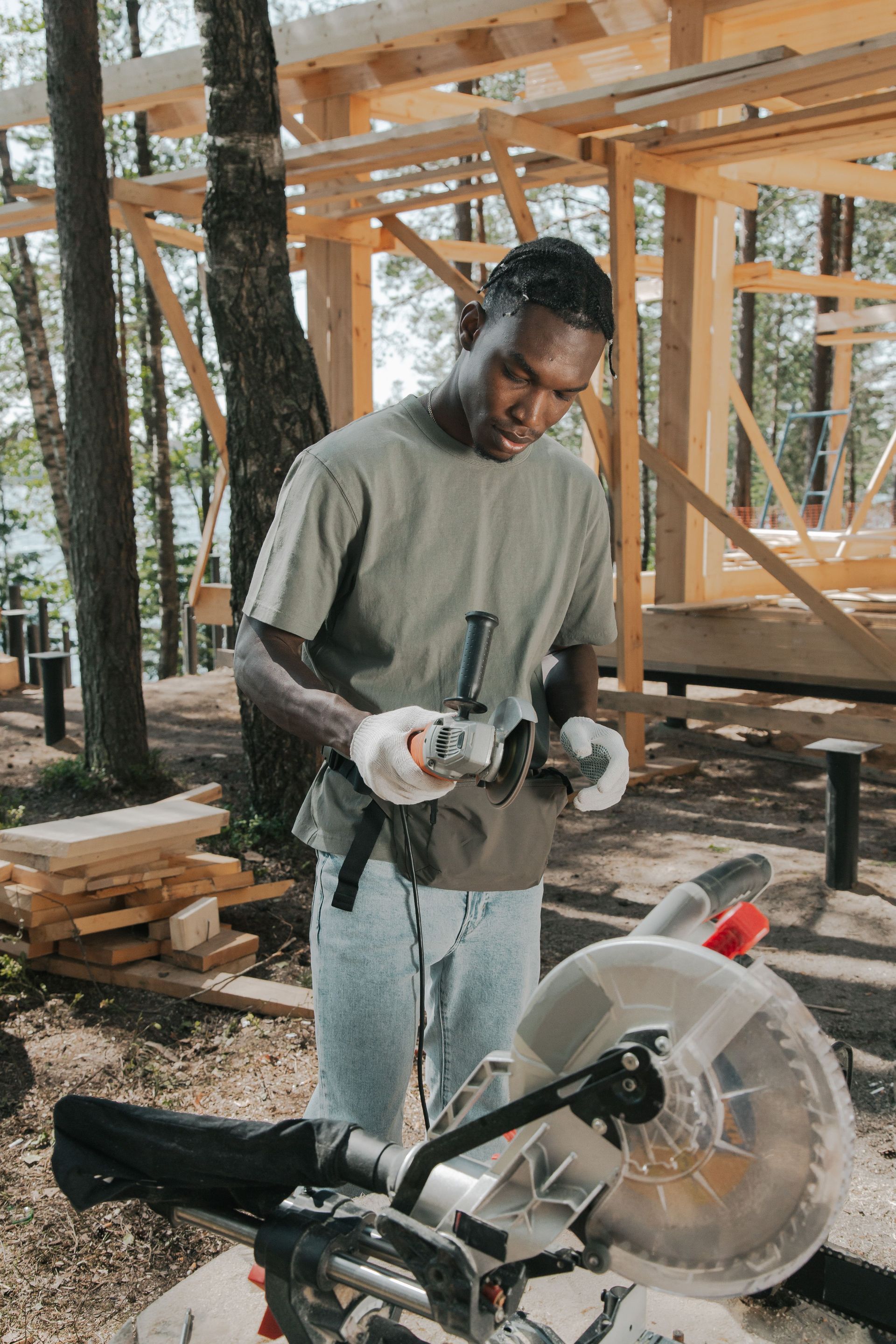 Person operating a circular saw at a wooden construction site, wearing gloves and a gray shirt.