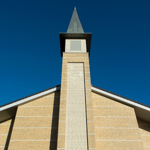 Brick church steeple with pointed roof against a clear blue sky