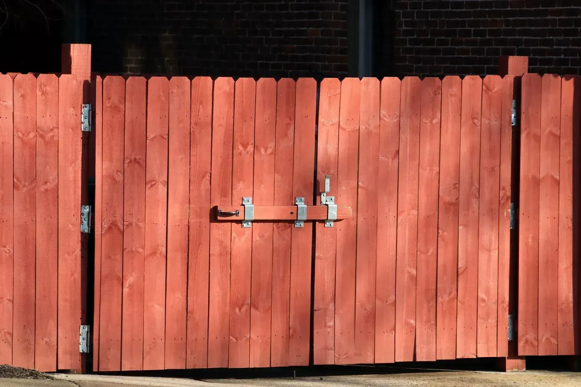 Red wooden double gate with metal latch in front of a brick wall