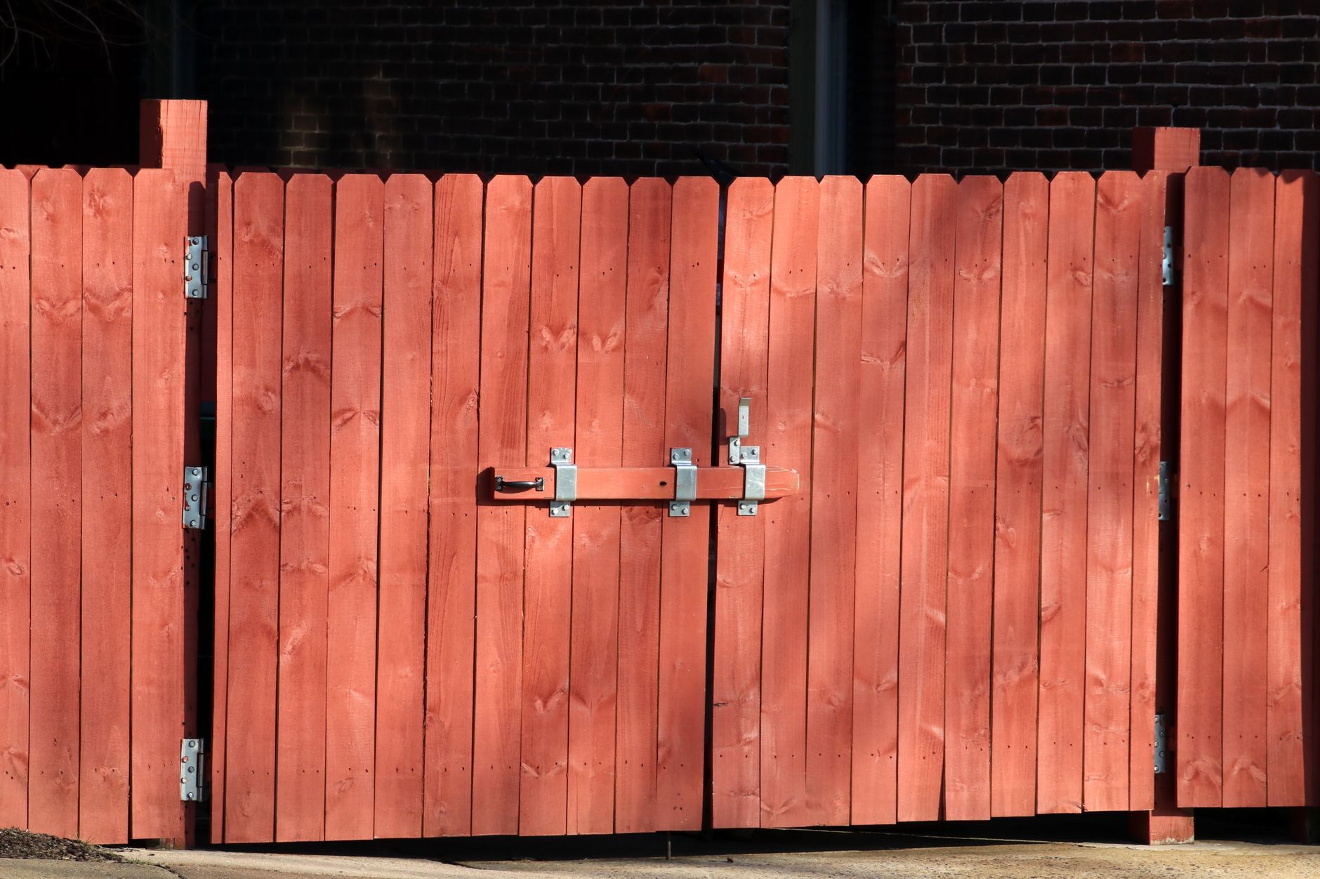 Red wooden double gate with metal latch in front of a brick wall