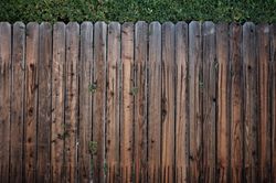 Weathered wooden fence with vertical slats, topped by green foliage.