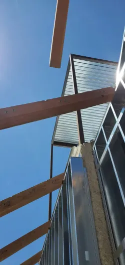 Low-angle view of a modern building with wooden beams and a metal roof against a blue sky