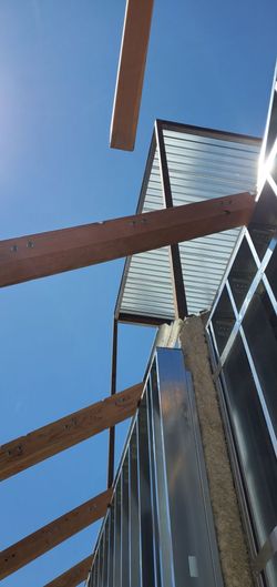 Low-angle view of a modern building with wooden beams and a metal roof against a blue sky