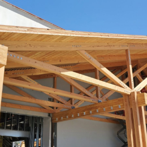 Wooden roof framing under construction against a blue sky, with exposed beams and trusses.
