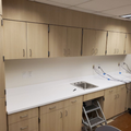 Empty kitchen workspace with light wood cabinets, white countertop, sink, and a step stool below the counter.