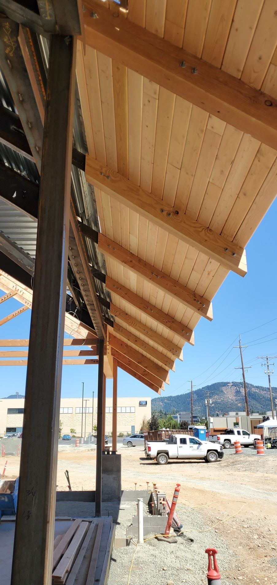 Wooden awning over a sidewalk with construction cones, parked trucks, and mountains in the distance