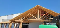 Construction site with exposed wooden roof trusses on a building under clear blue sky