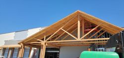 Construction site with exposed wooden roof trusses on a building under clear blue sky
