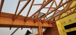 Wooden roof trusses over an unfinished building interior with yellow insulation wrap on the wall