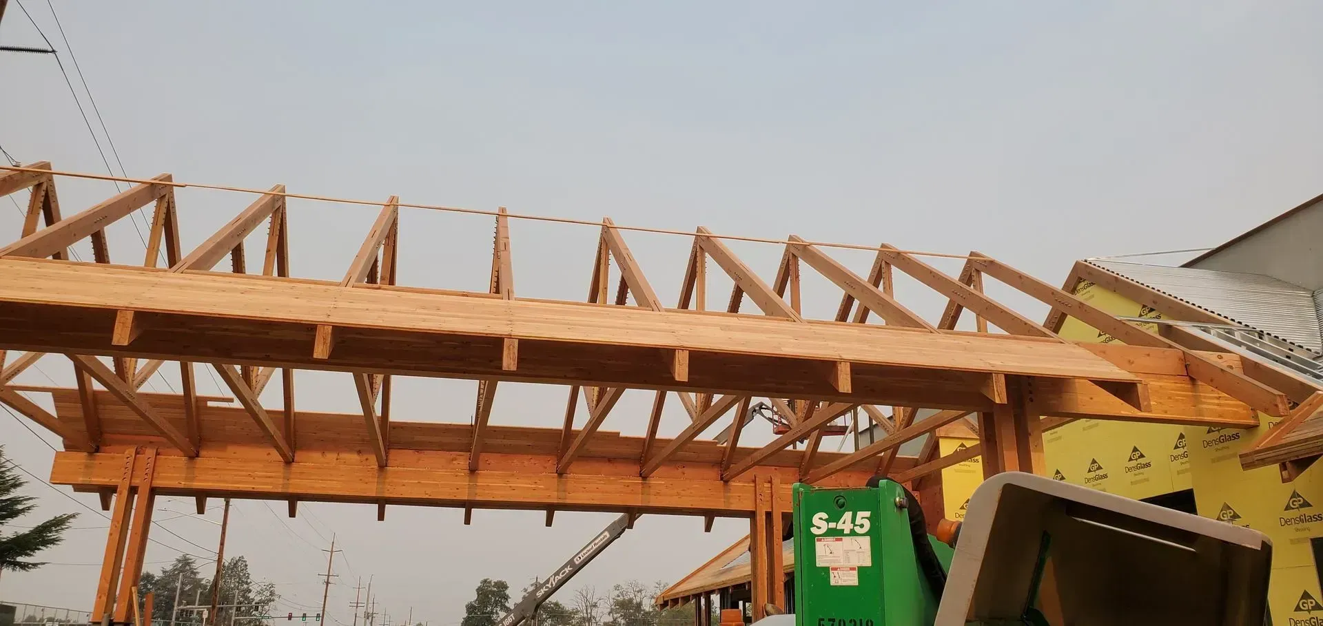 Wooden roof trusses being installed atop a building, with a green lift in the foreground.