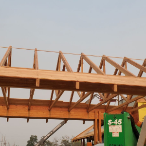 Wooden roof trusses being installed atop a building, with a green lift in the foreground.