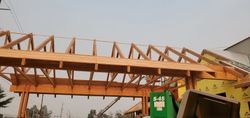 Damaged wooden roof trusses over an outdoor entrance, with a green sign and trees in the background