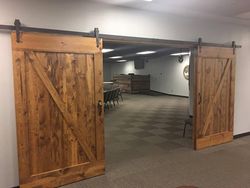Open wooden barn doors leading into a carpeted hall with tables and recessed lighting.