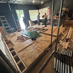 People building a raised floor in a dark room with ladders, lumber, and tools scattered around