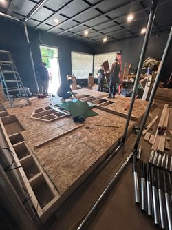 Indoor construction site with ladders, tools, and workers on a raised wooden platform