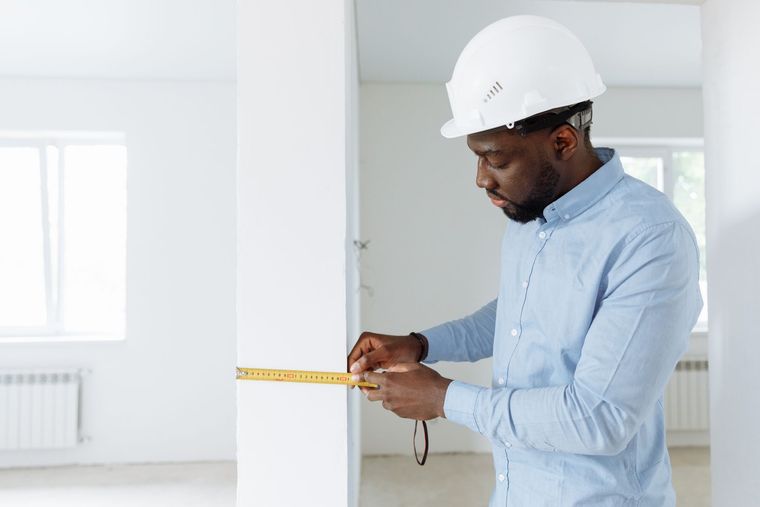 Construction worker measuring a white wall with a tape measure in a bright room