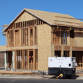 Framed two-story house under construction with plywood siding and a white generator in front