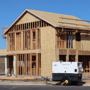 Framed two-story house under construction with plywood siding and a white generator in front