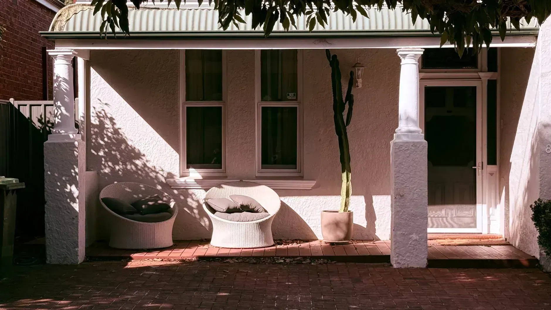 Front porch with white columns, potted plants, and a covered bench in front of a house