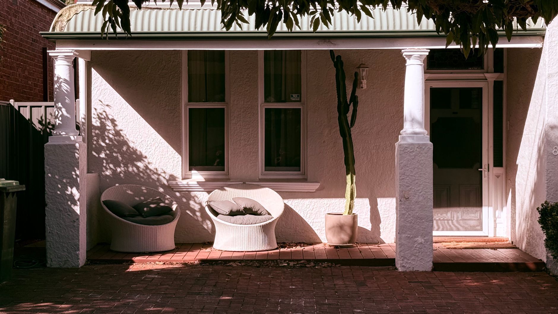 Front porch with white columns, potted plants, and a covered bench in front of a house