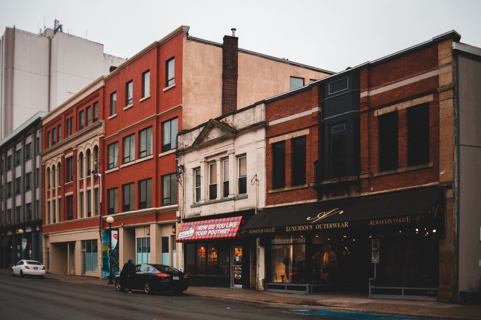 Old brick storefronts and apartments lining a wet city street on an overcast day