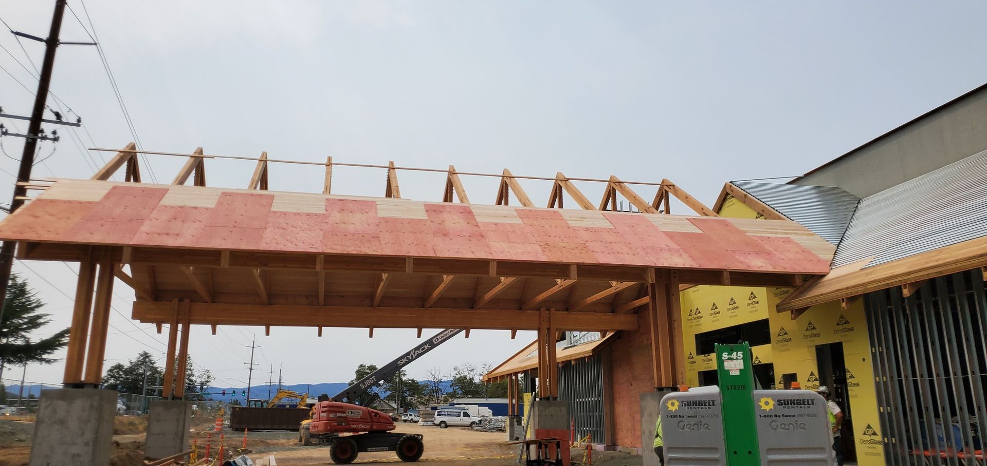 Partially built wooden pavilion with a pink roof over a construction site